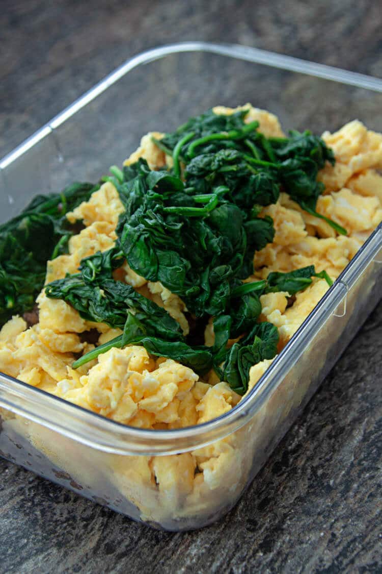browned sausage, scrambled eggs, wilted spinach in plastic storage container