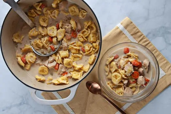 creamy chicken tortellini soup in a dutch oven on yellow placemat on marble background