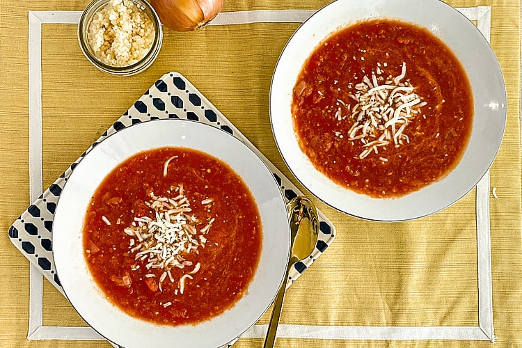 Garlic tomato soup in white bowls on a yellow placemat